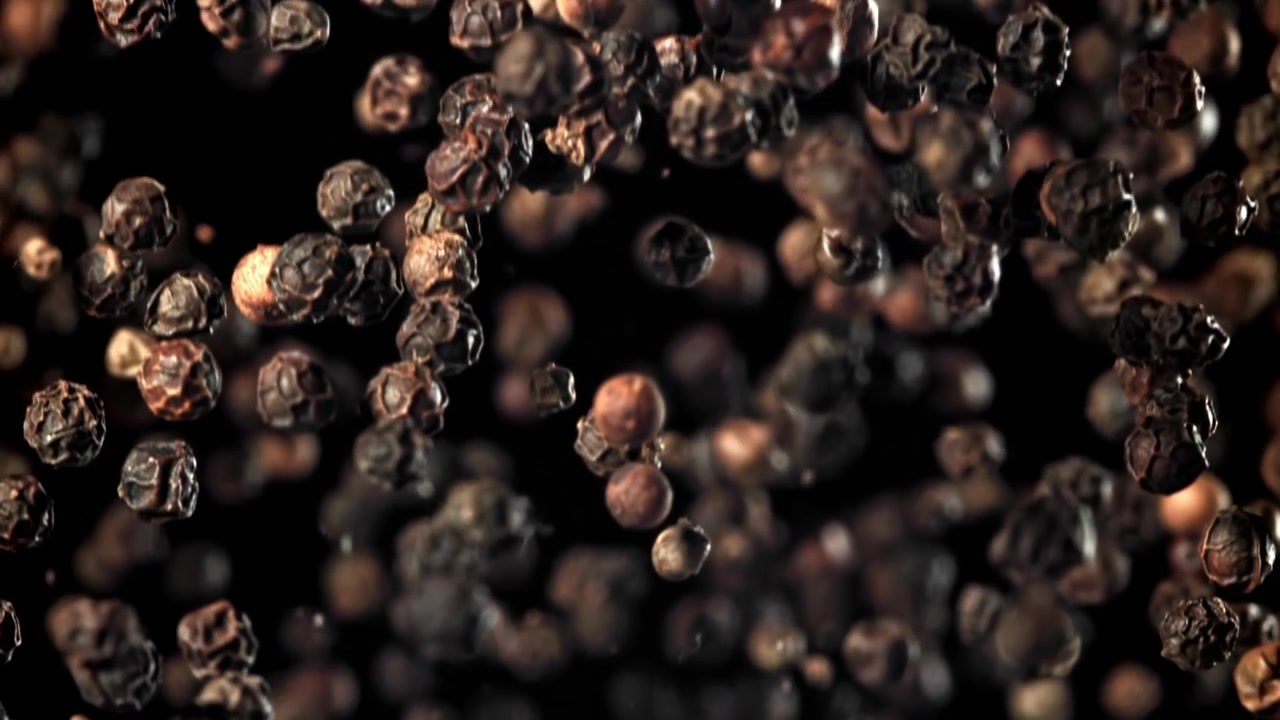 Svarte pepperkorn faller i super sakte film mot en mørk bakgrunn