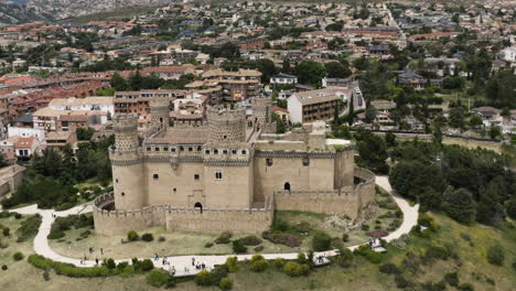 Antena-Sobre-El-Nuevo-Castillo-De-Manzanares-El-Real-Con-Una-Suave-Inclinación-Hacia-Arriba-Para-Revelar-La-Ciudad-Circundante-Y-Las-Impresionantes-Estribaciones-De-La-Sierra-De-Guadarrama