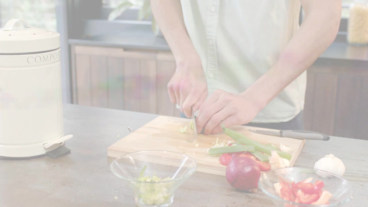 家庭で料理をする人が緑の野菜を置き、まな板の上で包丁で刻み、調理用にガラスのボウルに入れる。