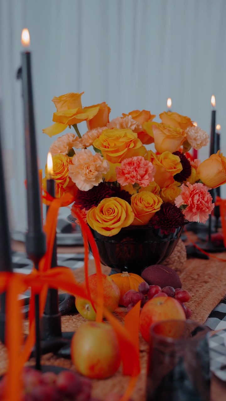 Centrotavola del Ringraziamento con candele accese, rose, garofani e frutta, allestito per una calda celebrazione festiva