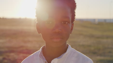 close-up-porträt eines kleinen afrikanisch-amerikanischen jungen, der ernsthaft nachdenklich in die kamera schaut. sonnenuntergang im strandpark. hintergrundlinsenflare