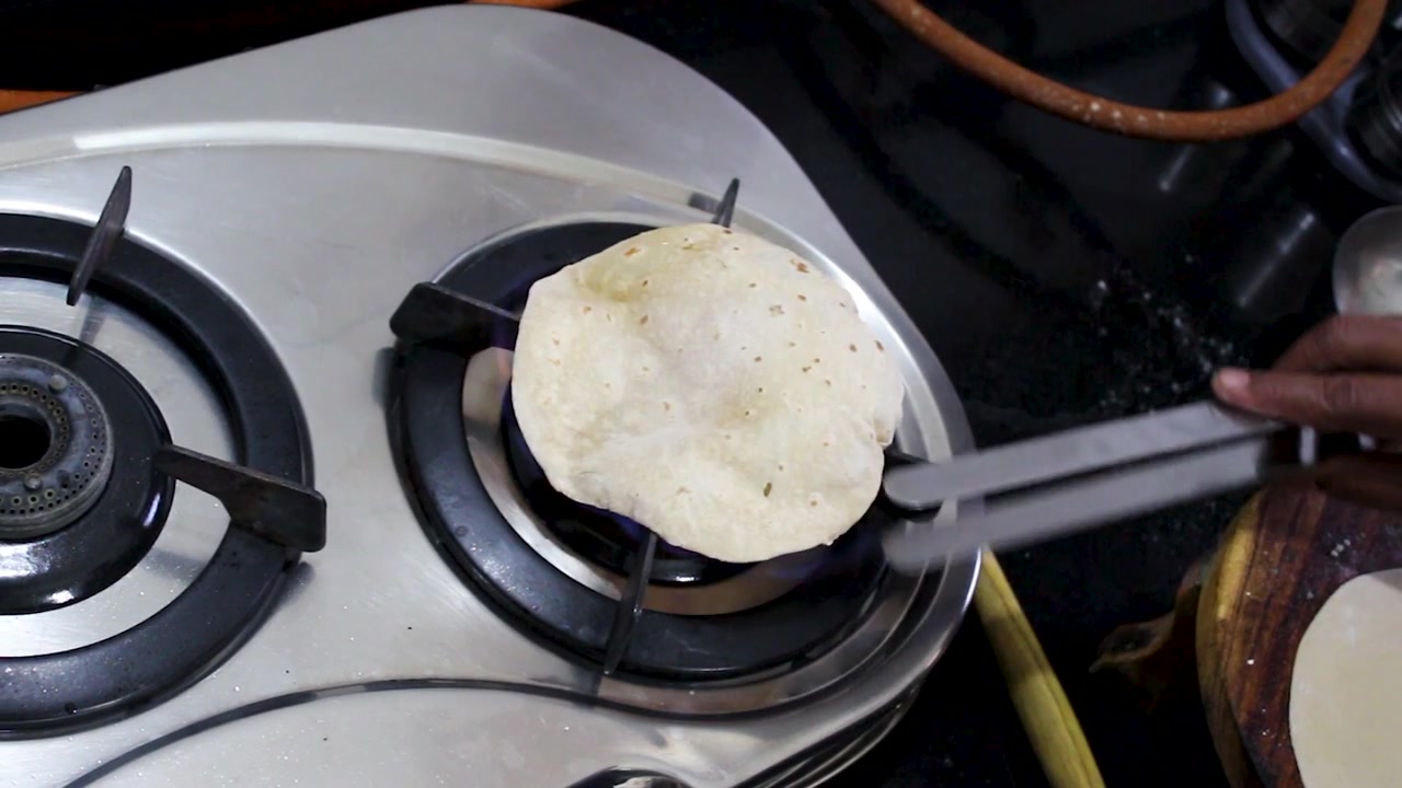 Filmato ravvicinato di chapati che si gonfiano su una fiamma a gas aperta in una cucina indiana. Autentica scena di cucina casalinga ideale per progetti di ricette, cultura culinaria e stile di vita domestico