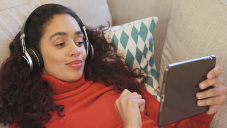 happy woman lying on sofa using tablet enjoying music on her headphones 4k 4k