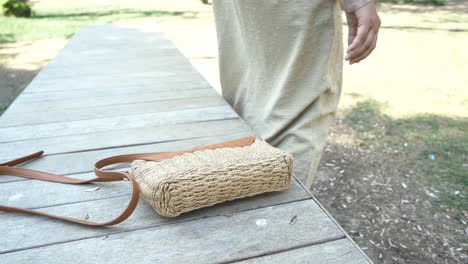 woman sitting on park bench with straw bag