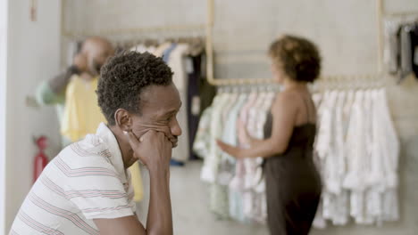 un chico negro aburrido esperando mientras su novio elige una camiseta.