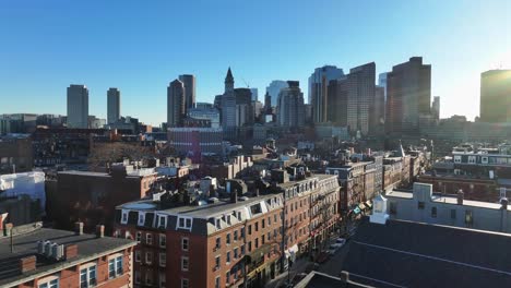 bustling boston skyline rises behind north end rowhouses. custom house tower stands tall among downtown skyscrapers. aerial during sunset.