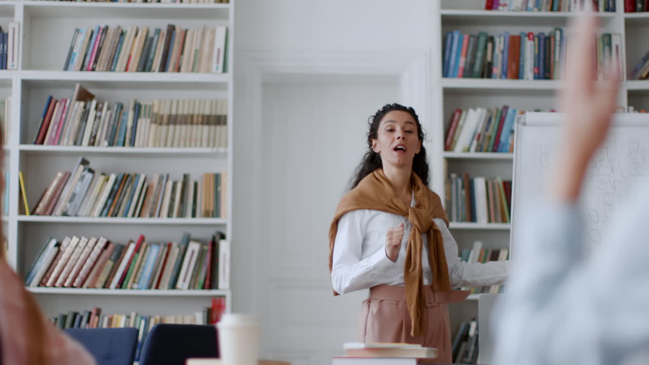 Female professor teaches a class, explaining concepts on a whiteboard in a library or classroom setting