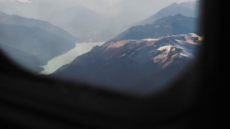 slow motion shot of mountains and lake through airplane window in flight