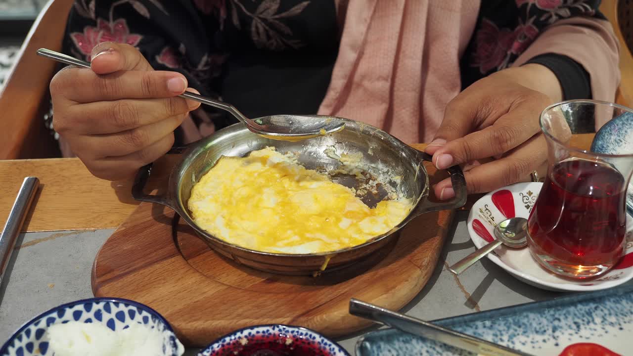 Woman eating breakfast of scrambled eggs and Turkish tea