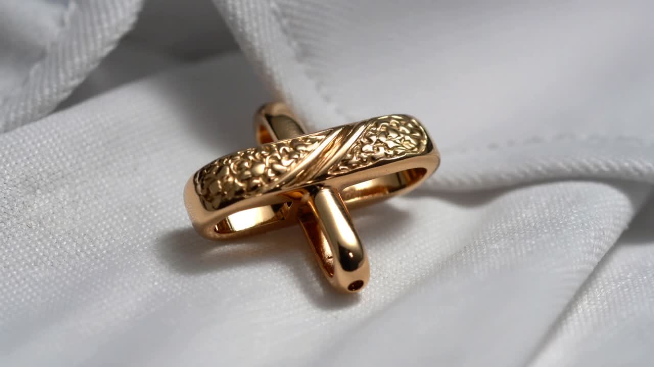 Rotating two interlocked gold rings on white cloth following frame change, revealing engraved band