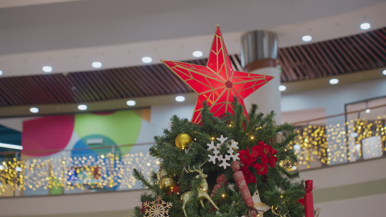 Close-up of beautifully decorated Christmas tree with glowing red star topper, golden ornaments, snowflakes, and festive decorations adorn lush green branches
