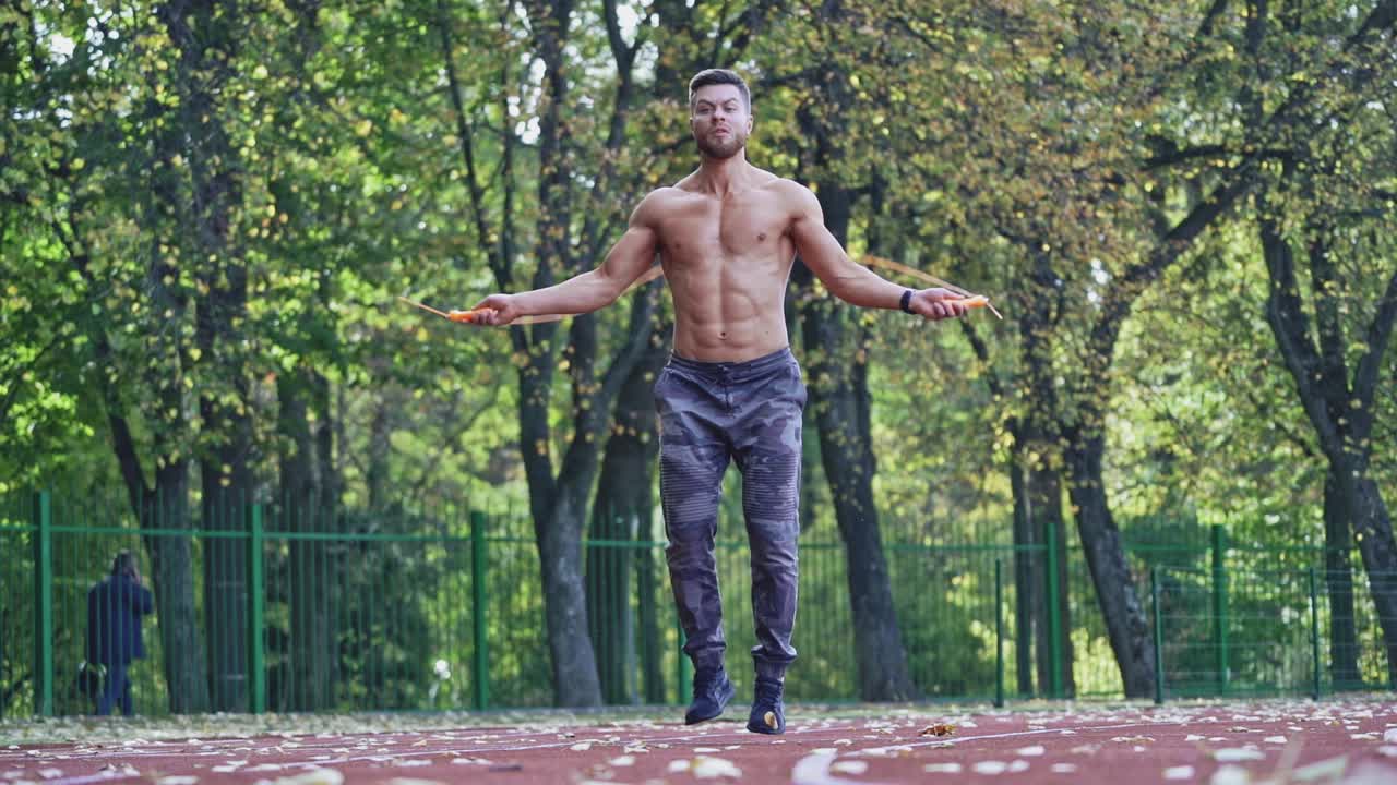 Athlete doing exercise at stadium. Active caucasian sportsman with skipping rope exercising on racetrack