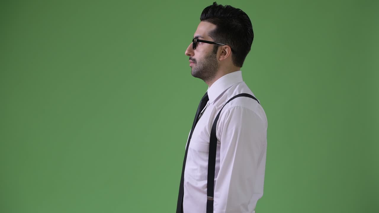 Young handsome bearded Persian businessman against green background