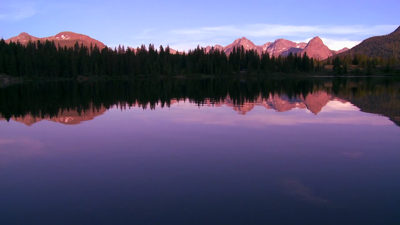 las montañas rocosas se reflejan perfectamente en un lago alpino al atardecer o al amanecer en esta toma itinerante 2