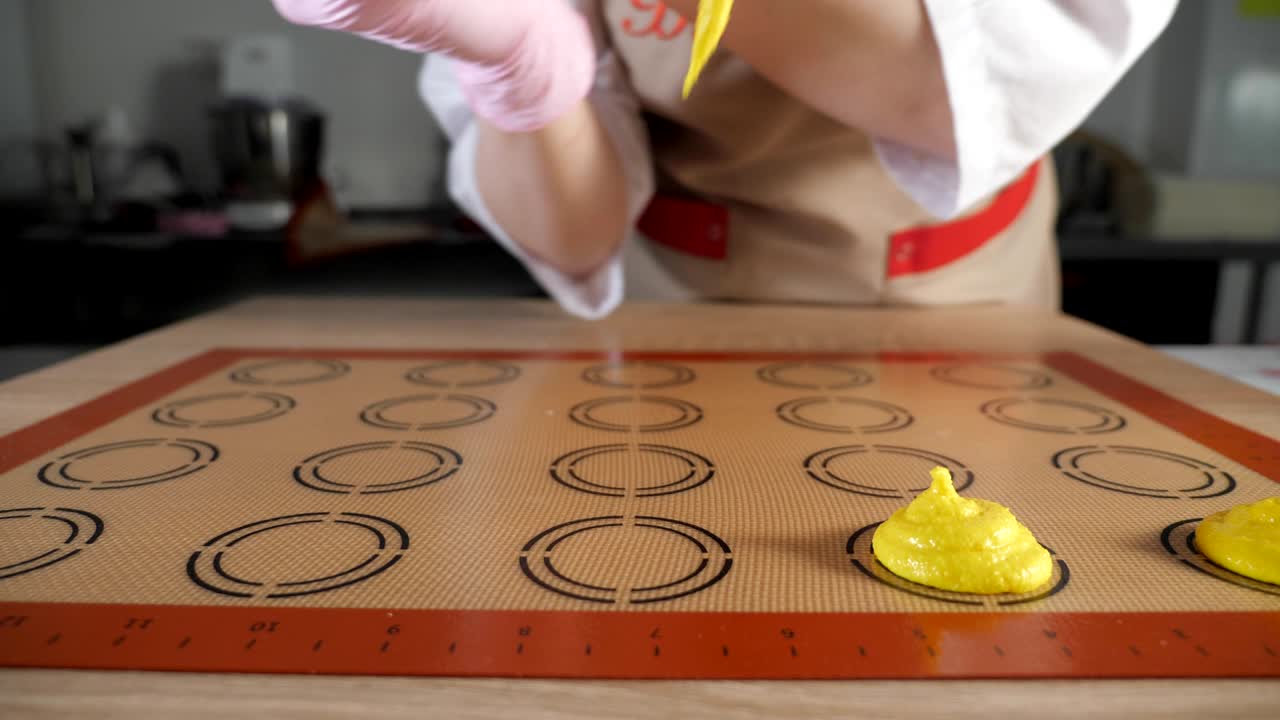페이스트리 셰프는 마카룬을 조리하고 있습니다. 스텐실 실리콘 매트에 반죽을 부어.