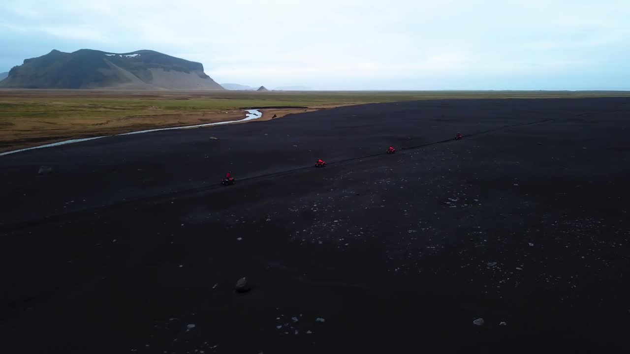 Aerial landscape view of bright red quad bikes speeding off road through Iceland black sand beach