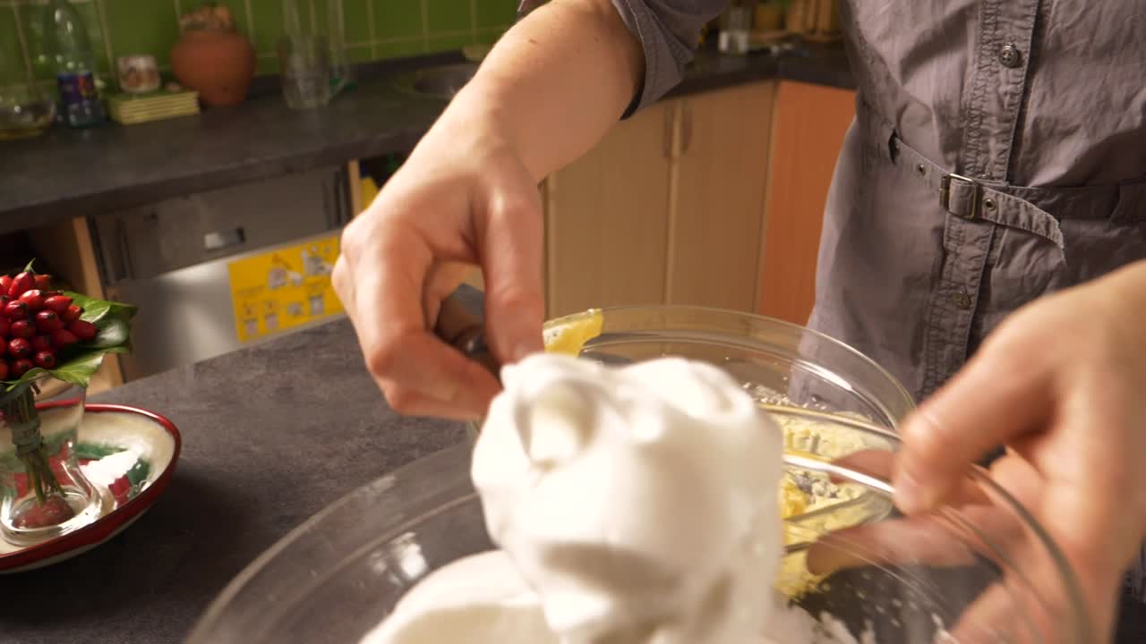 Toma en primer plano con zoom lento de una mujer joven mezclando la espuma de clara de huevo en la mezcla de mantequilla y miel, preparando un relleno de pastel de miel.
