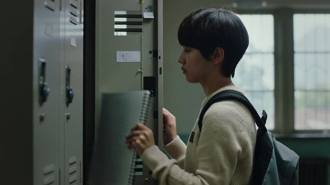 Reaching Asian student opening locker, taking notebook for class in hallway, wearing cream sweater