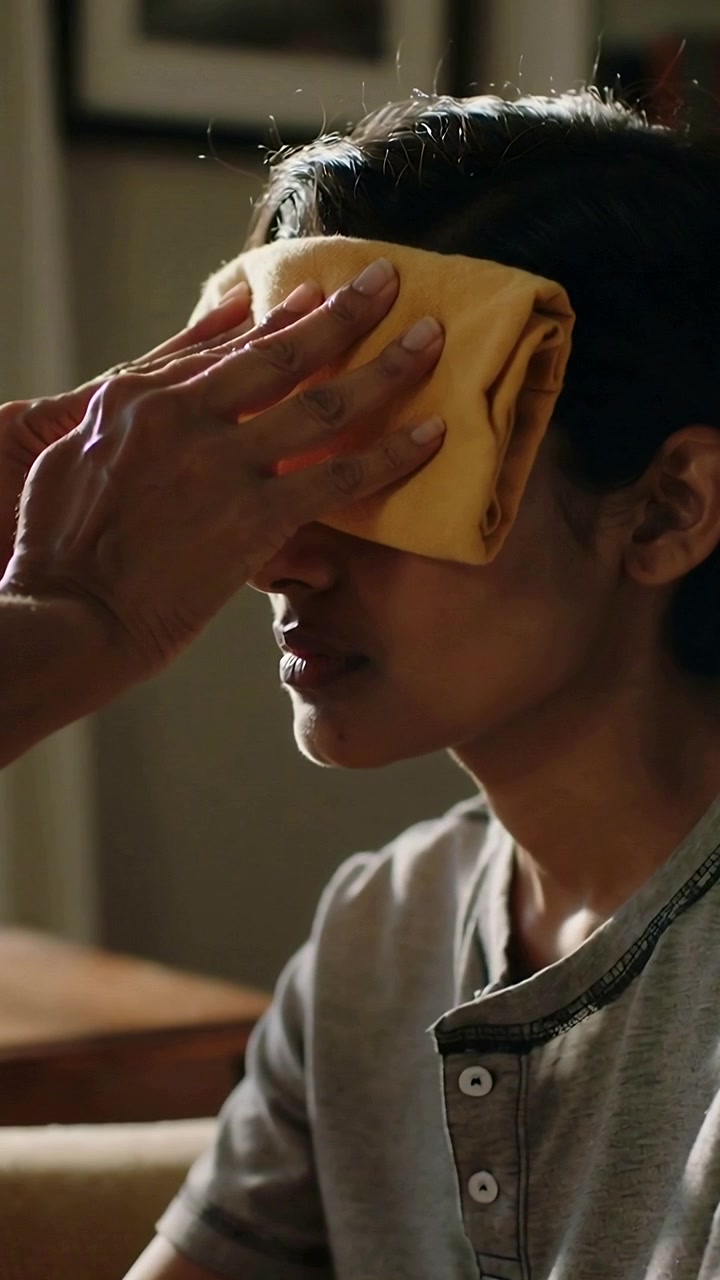 Vertical video: Reaching adult hand pressing yellow cloth over adolescent on couch