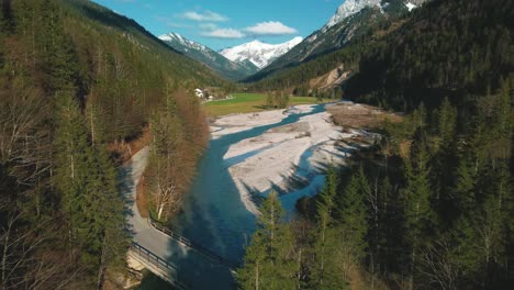 vuelo aéreo sobre un pintoresco río de montaña con agua azul fresca en los alpes bávaros austríacos por el sol de la tarde, fluyendo por un lecho de grava a lo largo de árboles, bosques y colinas vistos por drones