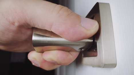 person turns metal knob and pulls to open white wooden door