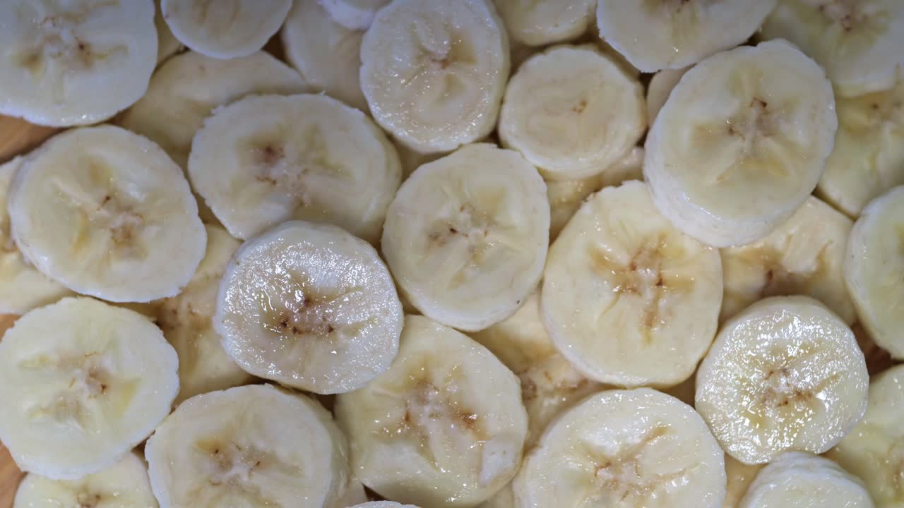 A close-up view of freshly sliced bananas spinning on a wooden surface. The slices appear moist and glistening, highlighting their natural texture and sweetness.