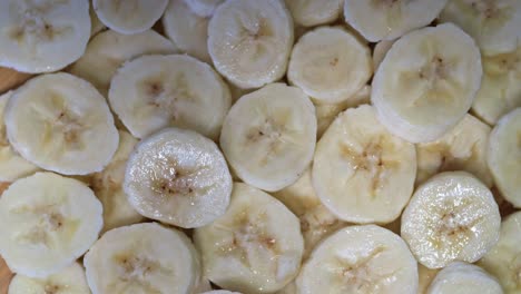 a close-up view of freshly sliced bananas spinning on a wooden surface. the slices appear moist and glistening, highlighting their natural texture and sweetness.