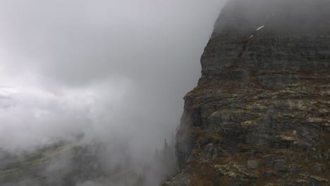 big mountain wall with clouds surrounding it, drone flying in to the clouds