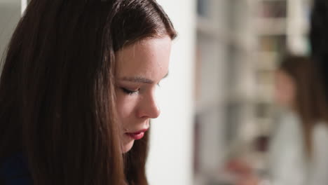 thoughtful woman in public library closeup. young reader looks down standing by rack in bookshop. student visits literature storage to learn materials