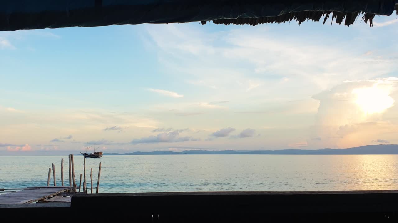 Ocean view with liveaboard boat from thatched roof accommodation hut on tropical island in Raja Ampat, West Papua Indonesia