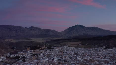 aerial view of a town nestled in a valley at twilight/sunrise with mountains in the background.