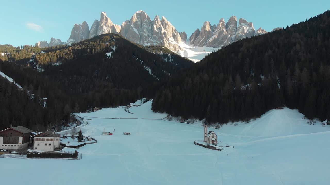 Aerial drone shot of Odle-Dolomites at sunset from Funes Tal with the famous St. John small church in snowy field, Val di Funes, Southyrol. Zoomed in post for a more dynamic video