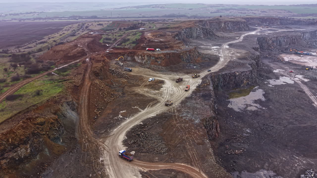 Granite quarry operations in an open pit area with machinery and vehicles engaged in material extraction and transportation