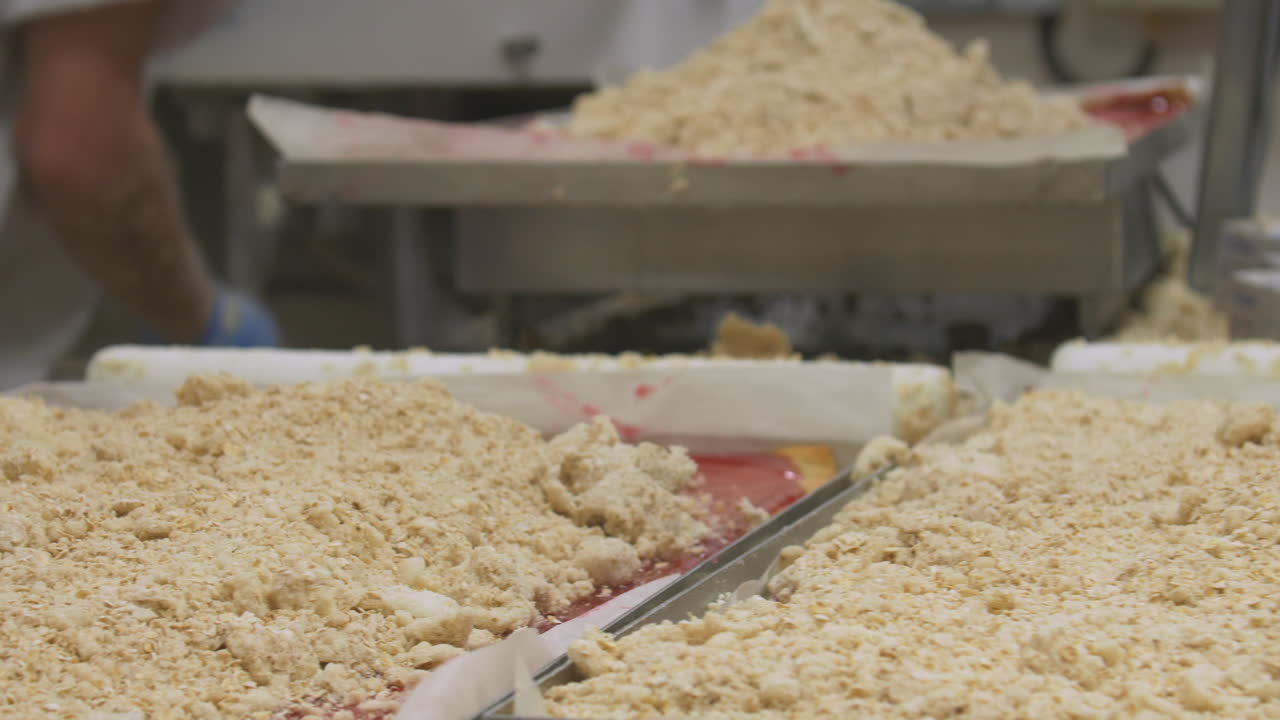 Pan from left to right of workers preparing crumble cake so the topping covers the tray evenly