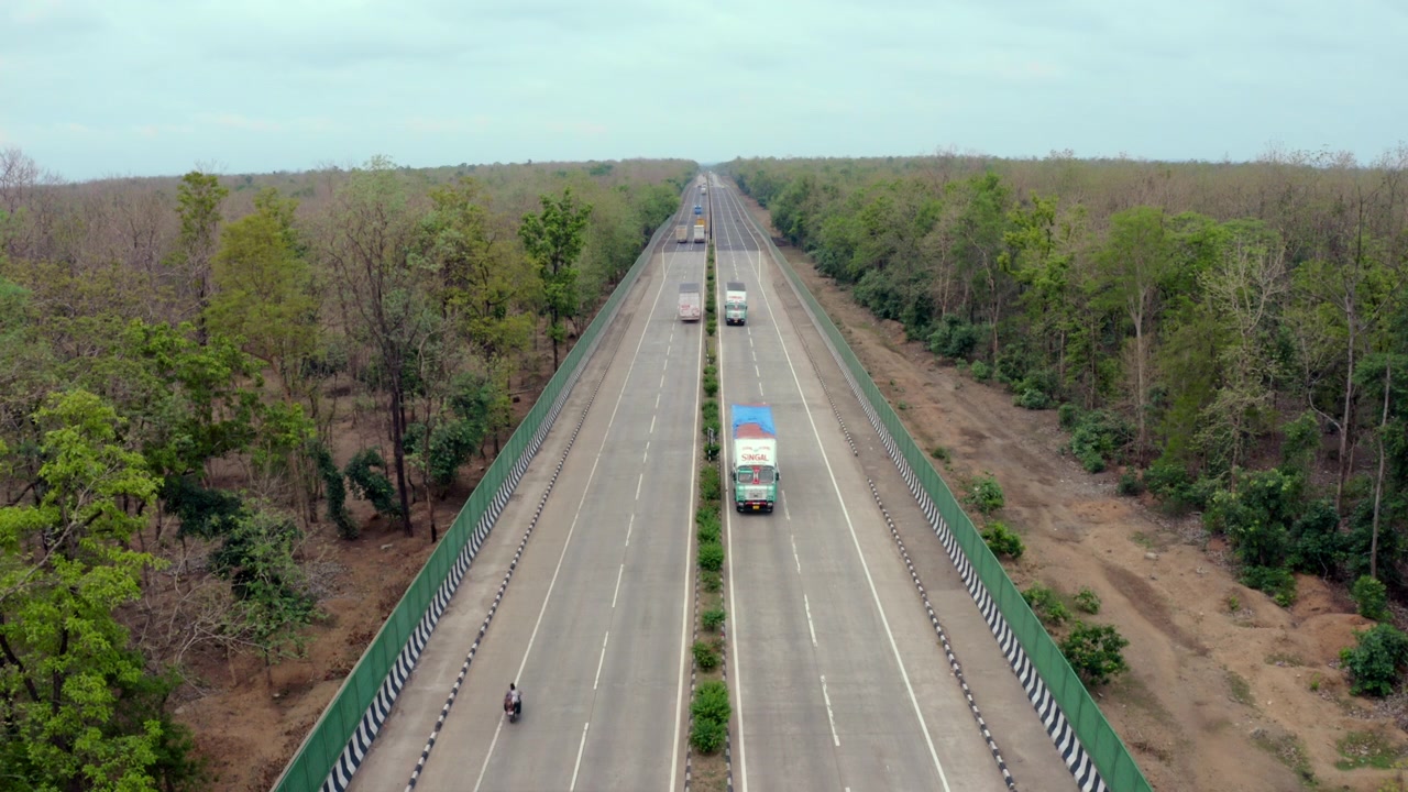 Veduta aerea del traffico e dei veicoli che percorrono la Strada Statale 44 (NH 44) attraverso una fitta foresta in India, ripresa in tracking con drone, 4K.