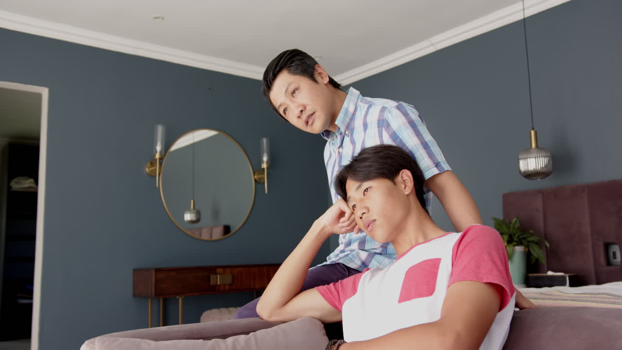 asian father and son sitting on couch, having serious conversation at home