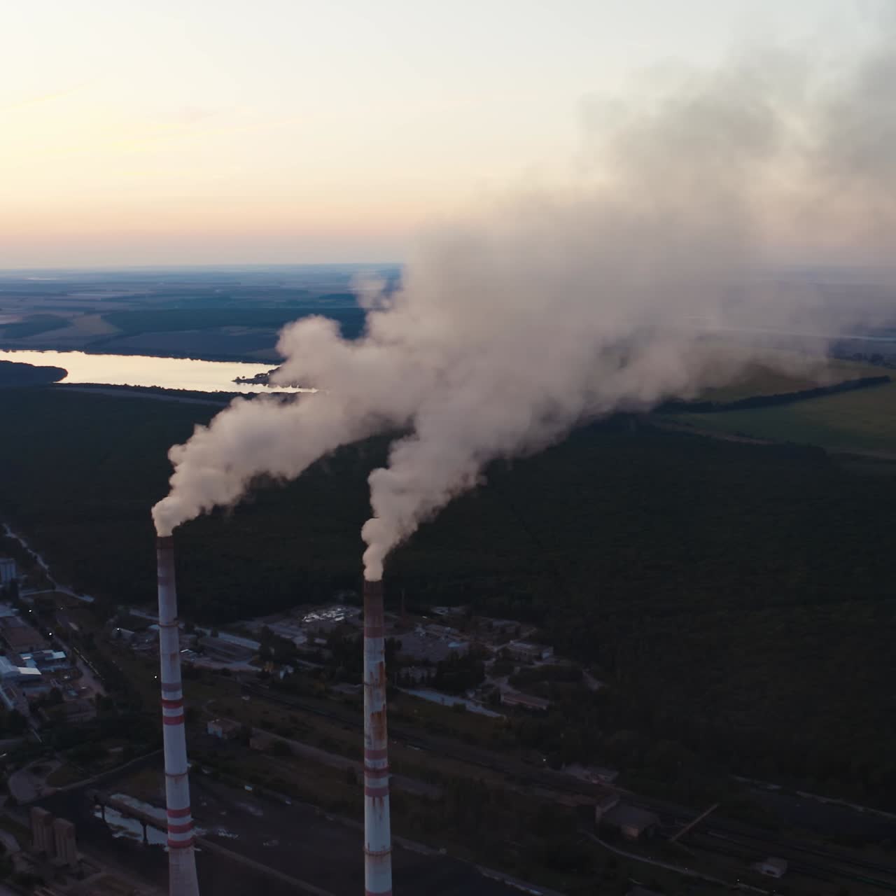 White smoke from pipes in the natural environment. Industrial factory near the beautiful river in the countryside in the evening. Air pollution.