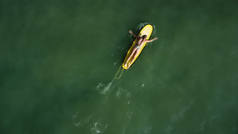 aerial top down, surfer girl paddling surfboard on calm ocean water