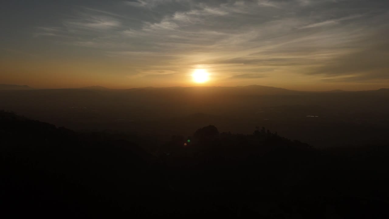 A static shot of a foggy sun above mountains, casting a smooth yellow light across the horizon.