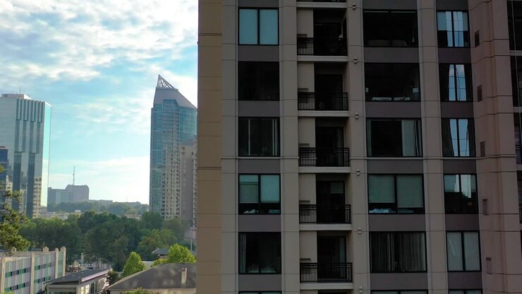 Cena de drone em movimento lento voando por trás de um arranha-céu, revelando o centro de Buckhead e outros prédios altos ao fundo