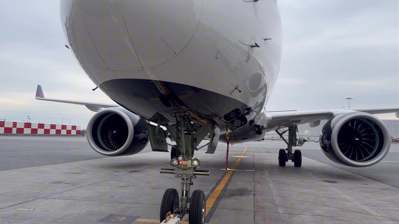 Ripresa a livello del suolo con panoramica dal carrello anteriore dell'Airbus A220 verso l'alto, con il motore numero 2 in funzione al gate dell'aeroporto. Perfetto per progetti di aviazione, aerospaziali, compagnie aeree e tecnici.