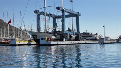 turkey,marmaris, marina, first smaller crane is pulling a boat from the dock and moving than the bigger crane is pulling a bugger boat out of the water and moving the boat to the land on a sunny day.