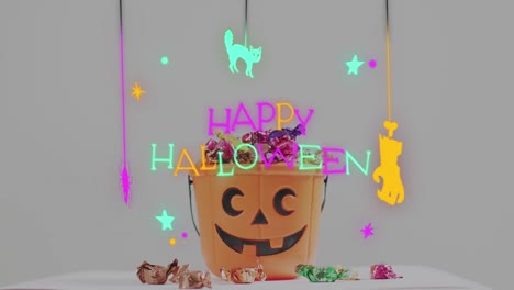 neon happy halloween text banner against pumpkin shaped bucket full of halloween candies