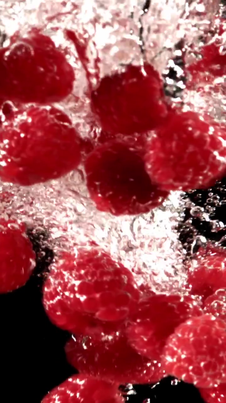 Fresh Red Raspberries Falling into Clear Water with Bubbles