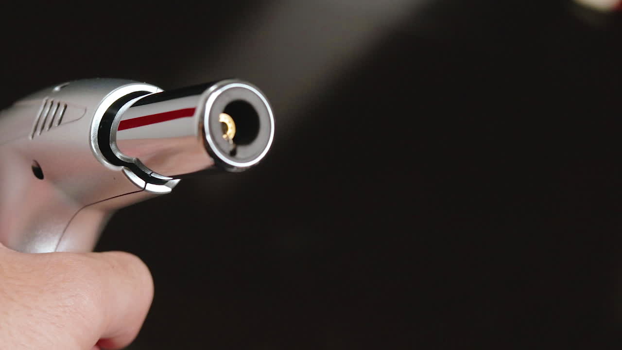 mano masculina sosteniendo y usando soplete frente a la cámara sobre un fondo oscuro, primer plano en la punta