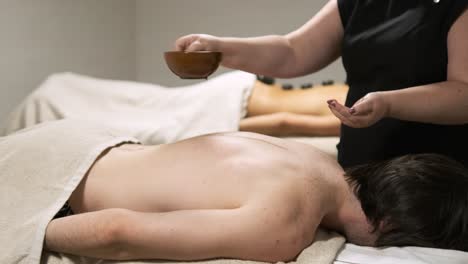 masseuse gently pouring massage oil on a man's back for relaxation