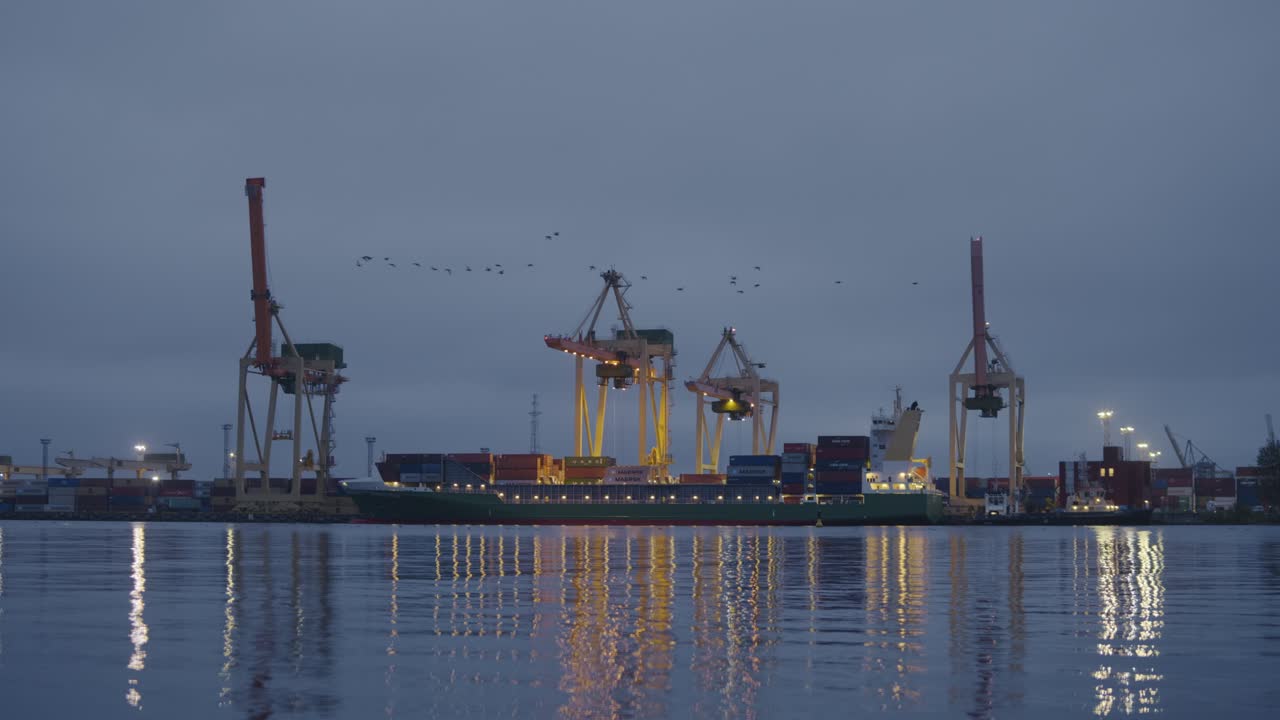 Soft sunrise reflections shimmer across calm Riga harbor as cranes stand tall
