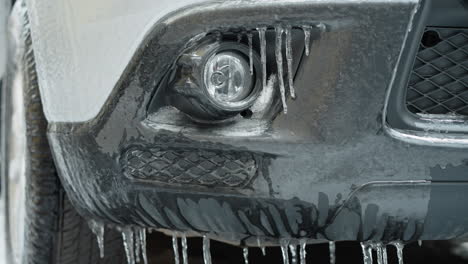 detailed close-up of a car's fog light encased in ice with icicles, showing the harsh winter conditions and their effect on vehicle exteriors