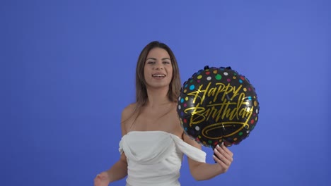 una joven vestida de blanco posa con un globo de feliz cumpleaños negro
