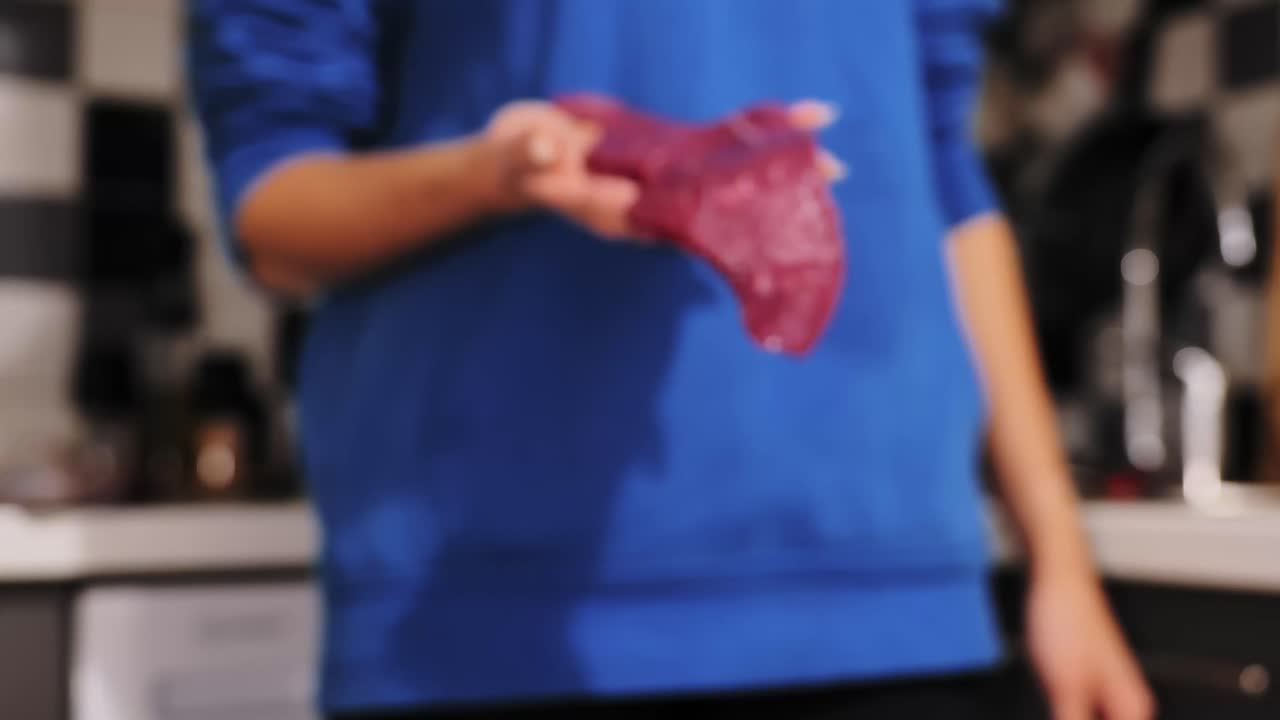 Evening kitchen with woman holding raw steak toward lens under soft warm light